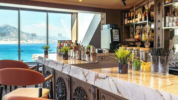 Un espace bar doté d’un comptoir en marbre, de plantes en pot et offrant une vue sur la mer.