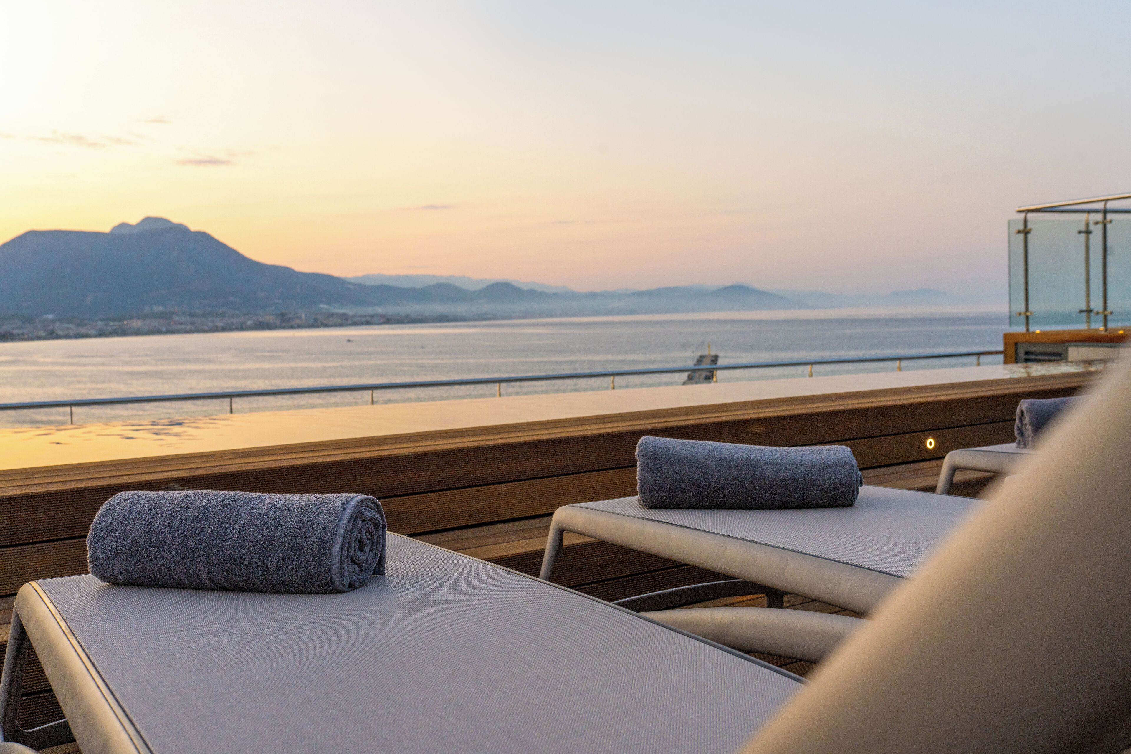 A sunlit terrace with lounge chairs and a view of the sea and mountains.