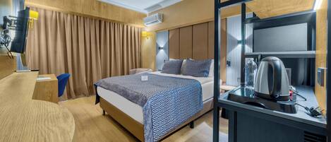 A hotel room with a bed, bedside table, and a desk with a kettle.