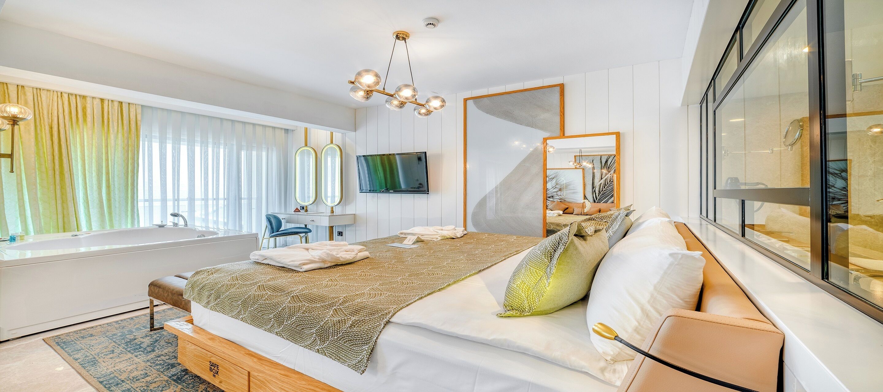 A modern bedroom with a large bed, a desk, a TV, and a large window with curtains.