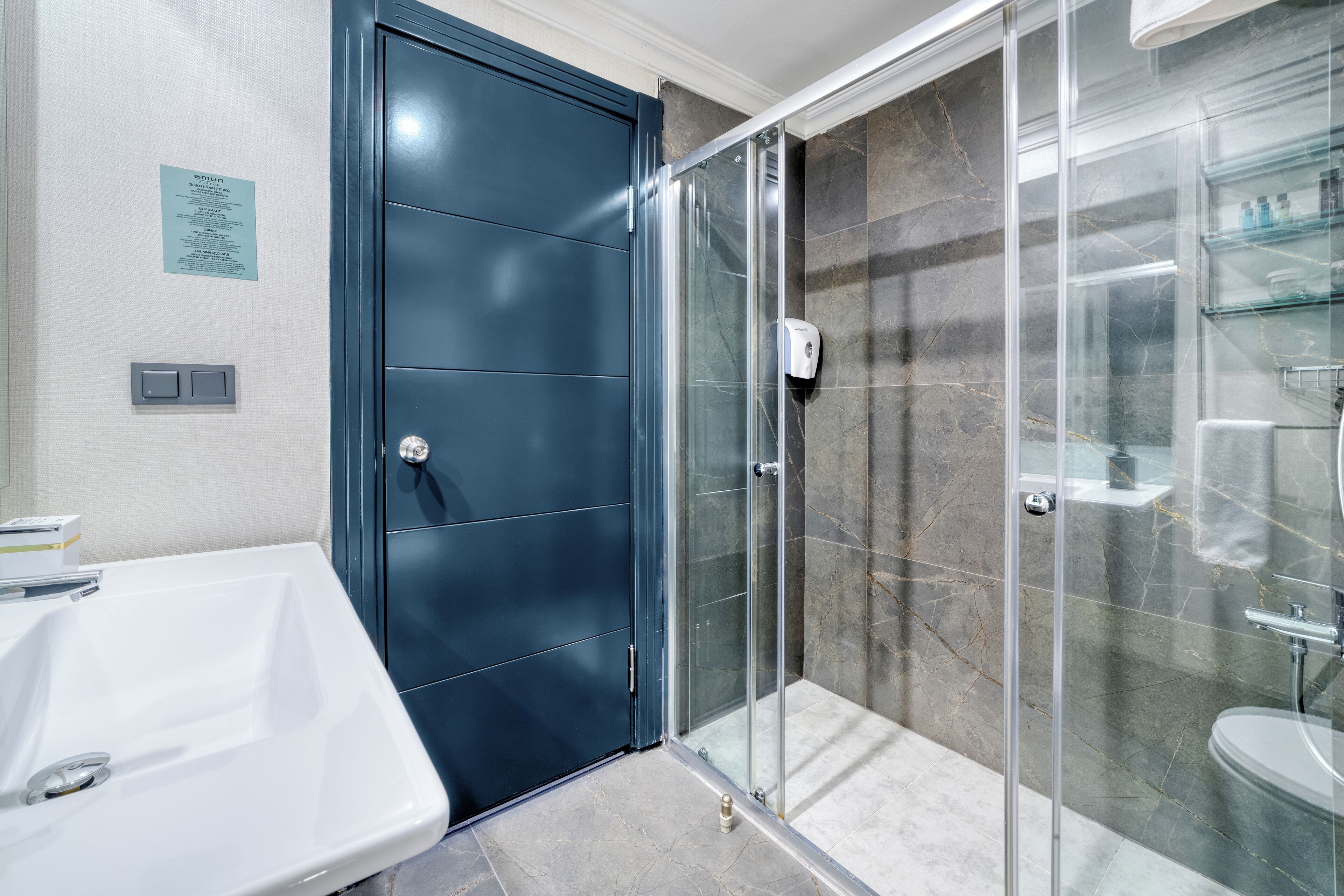A modern bathroom with a glass-enclosed shower, a white sink, and a dark blue door.