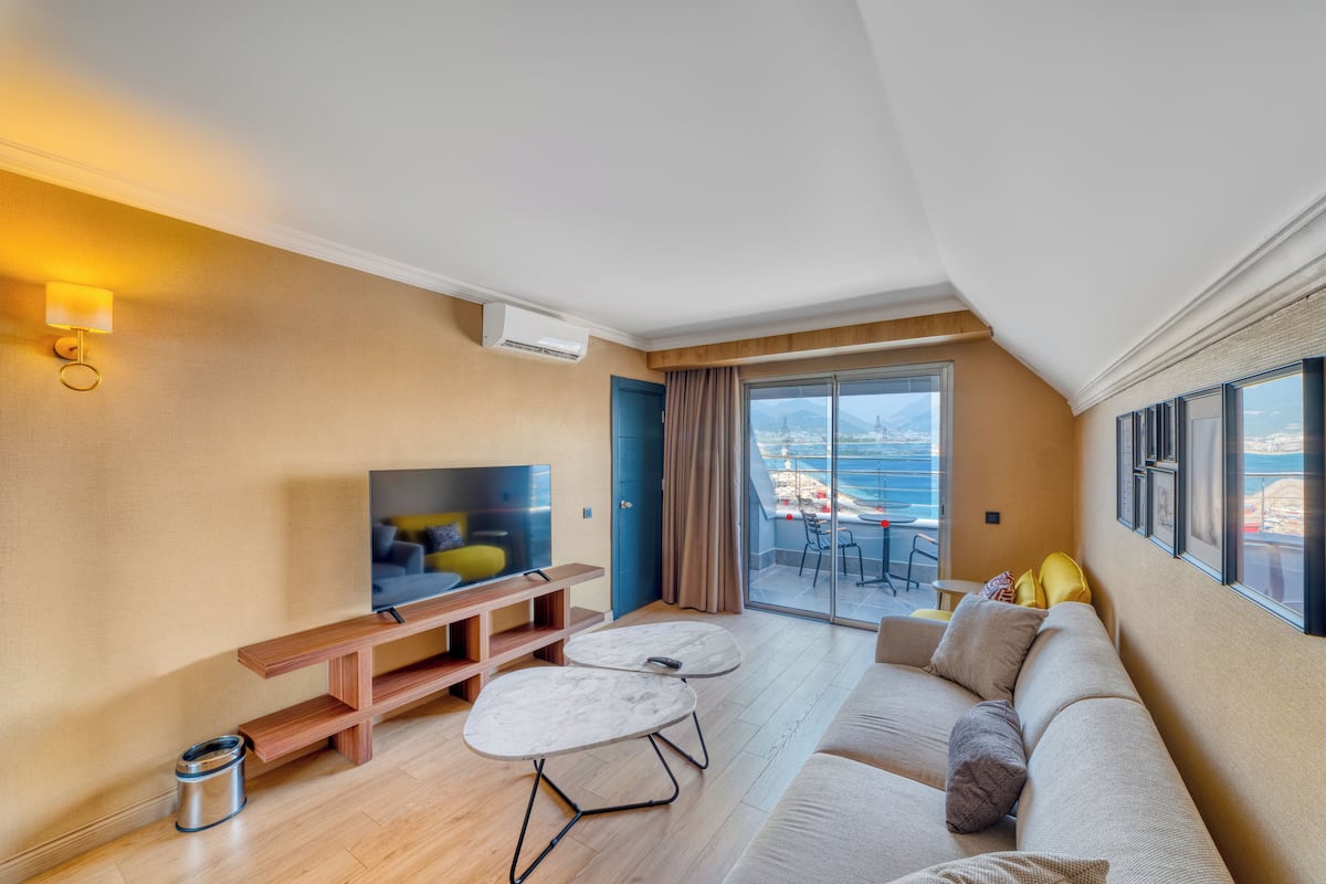 A modern living room with a sofa, coffee table, TV, and a balcony with a view of the sea.