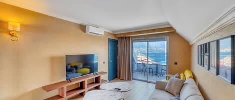 Un salon moderne avec un canapé, une table basse, un téléviseur et un balcon offrant une vue sur la mer.