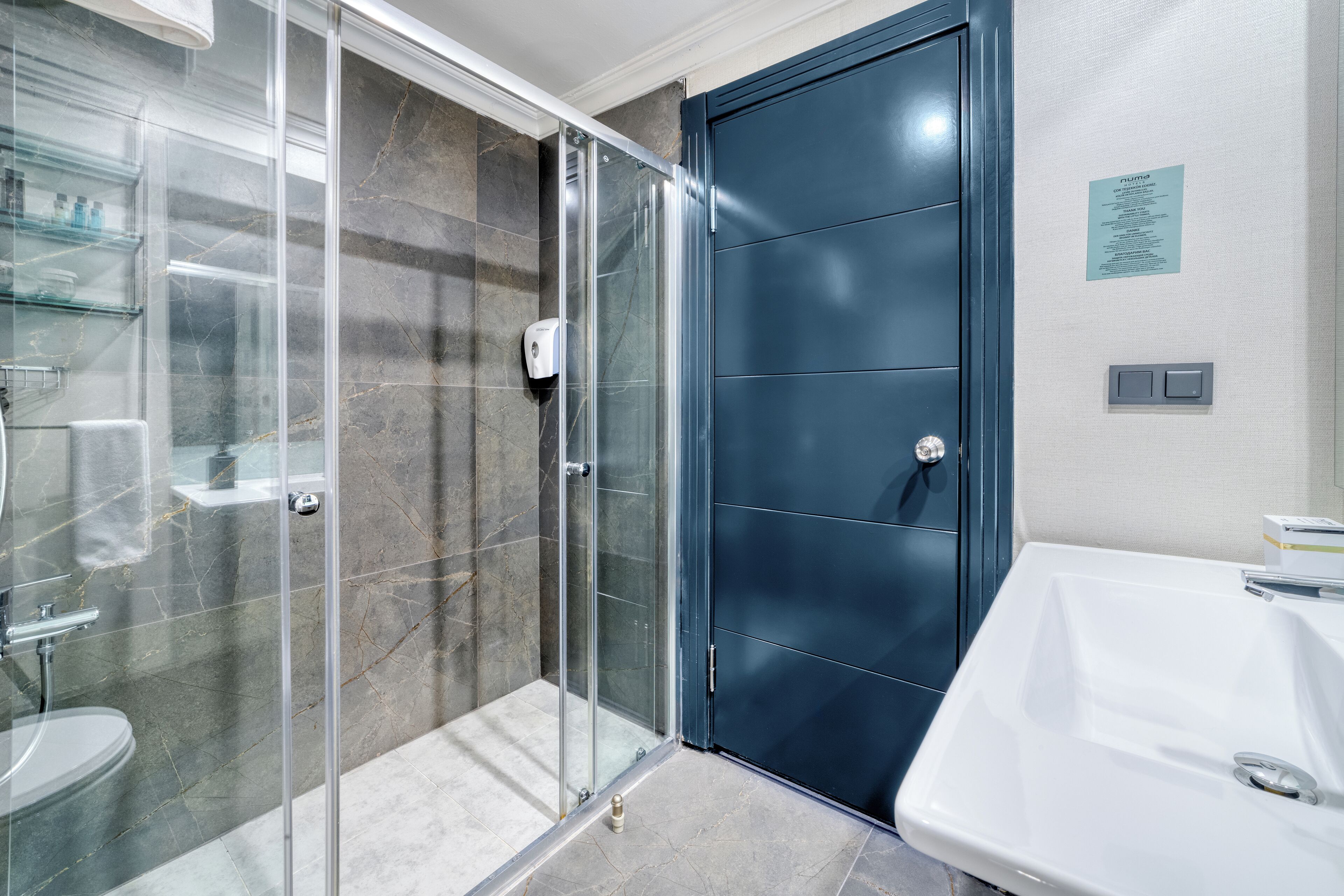 A modern bathroom with a glass-enclosed shower, a dark blue door, and a white sink.