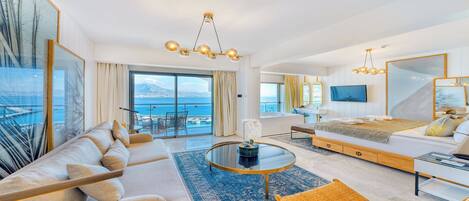 A modern hotel room with a large bed, a sofa, a dining area, and a balcony with a view of the sea.