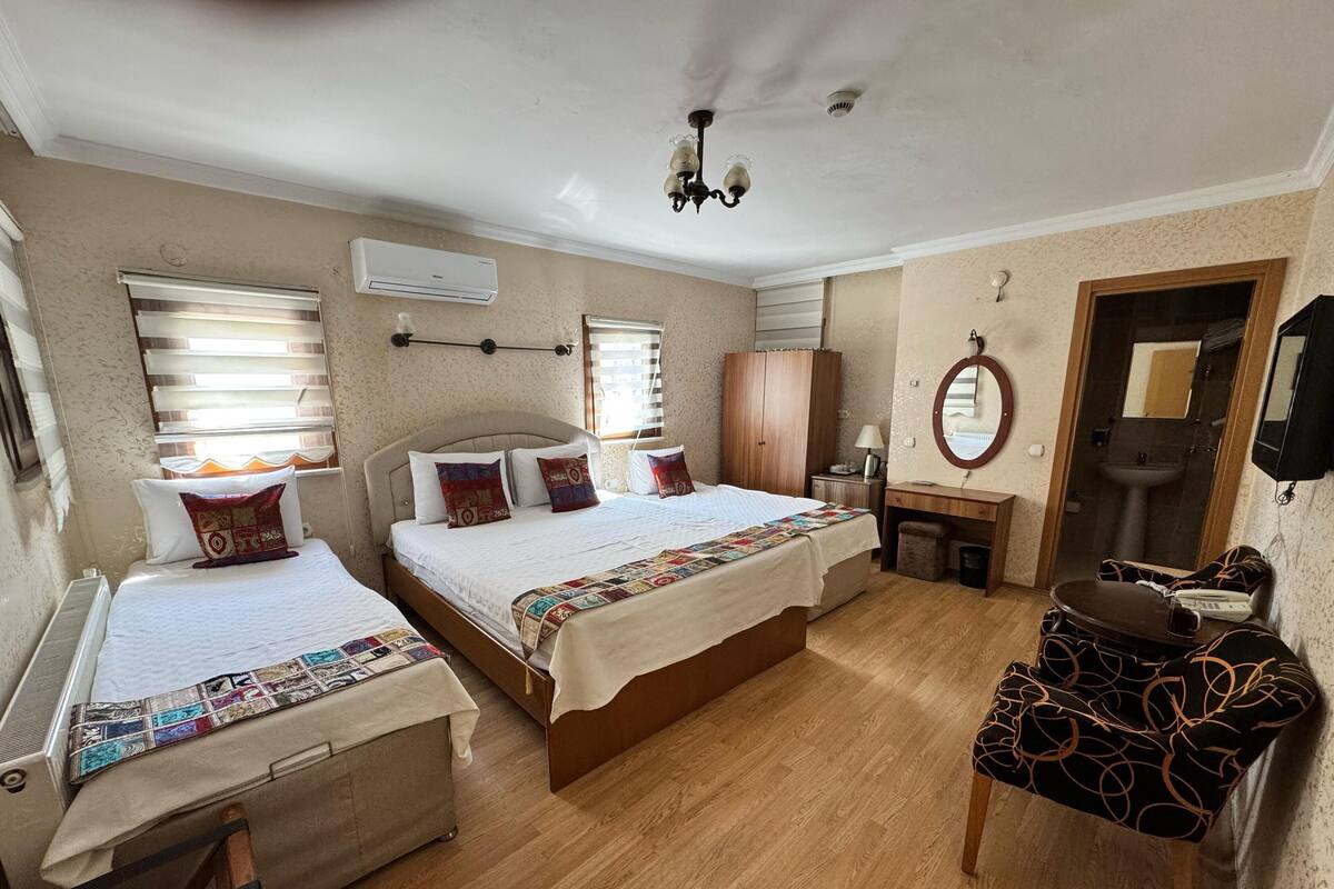 Habitación de hotel con dos camas, un escritorio de madera, un espejo, un radiador y un ventilador de techo.