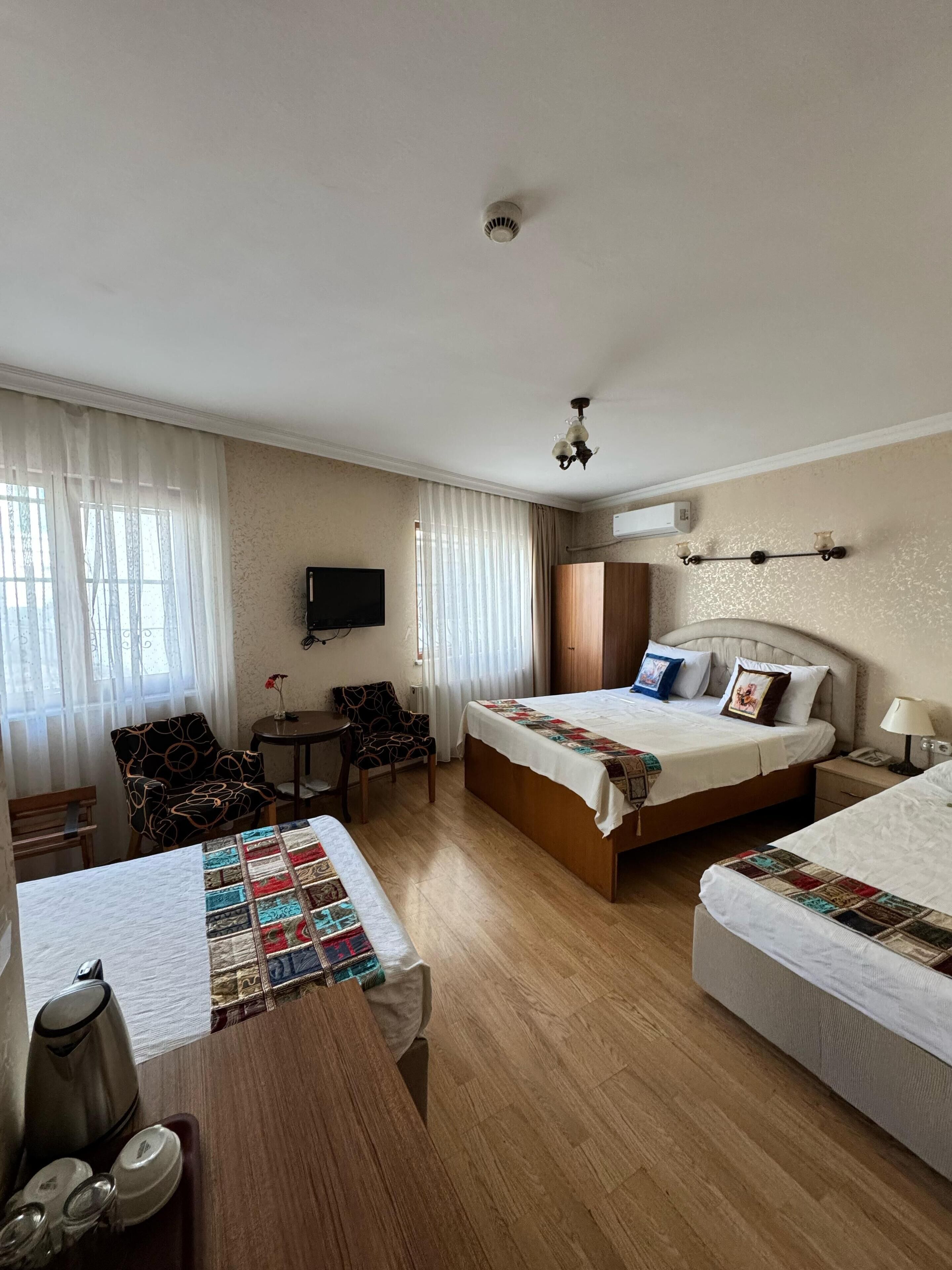 Habitación de hotel con dos camas, un escritorio, una silla, un televisor y una ventana con cortinas.