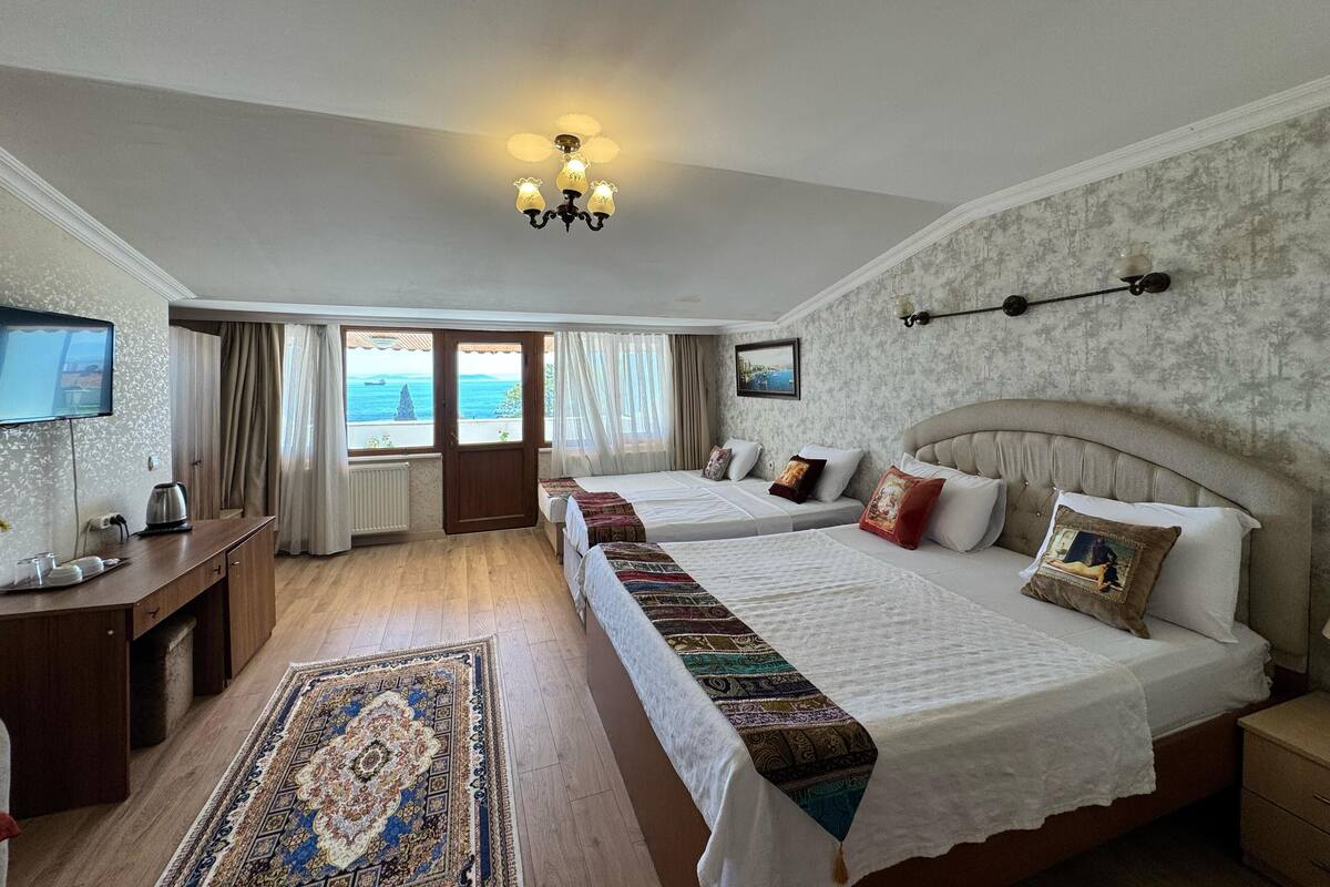 Habitación de hotel con dos camas, un escritorio con hervidor, televisión y vista al mar.