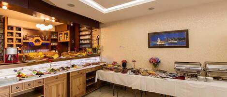 Una mesa de buffet con diversos platos y bebidas, una máquina de café y un cuadro en la pared.