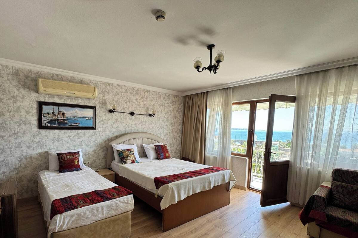 Habitación de hotel con dos camas, ventilador de techo, candelabro, vista al mar y balcón.