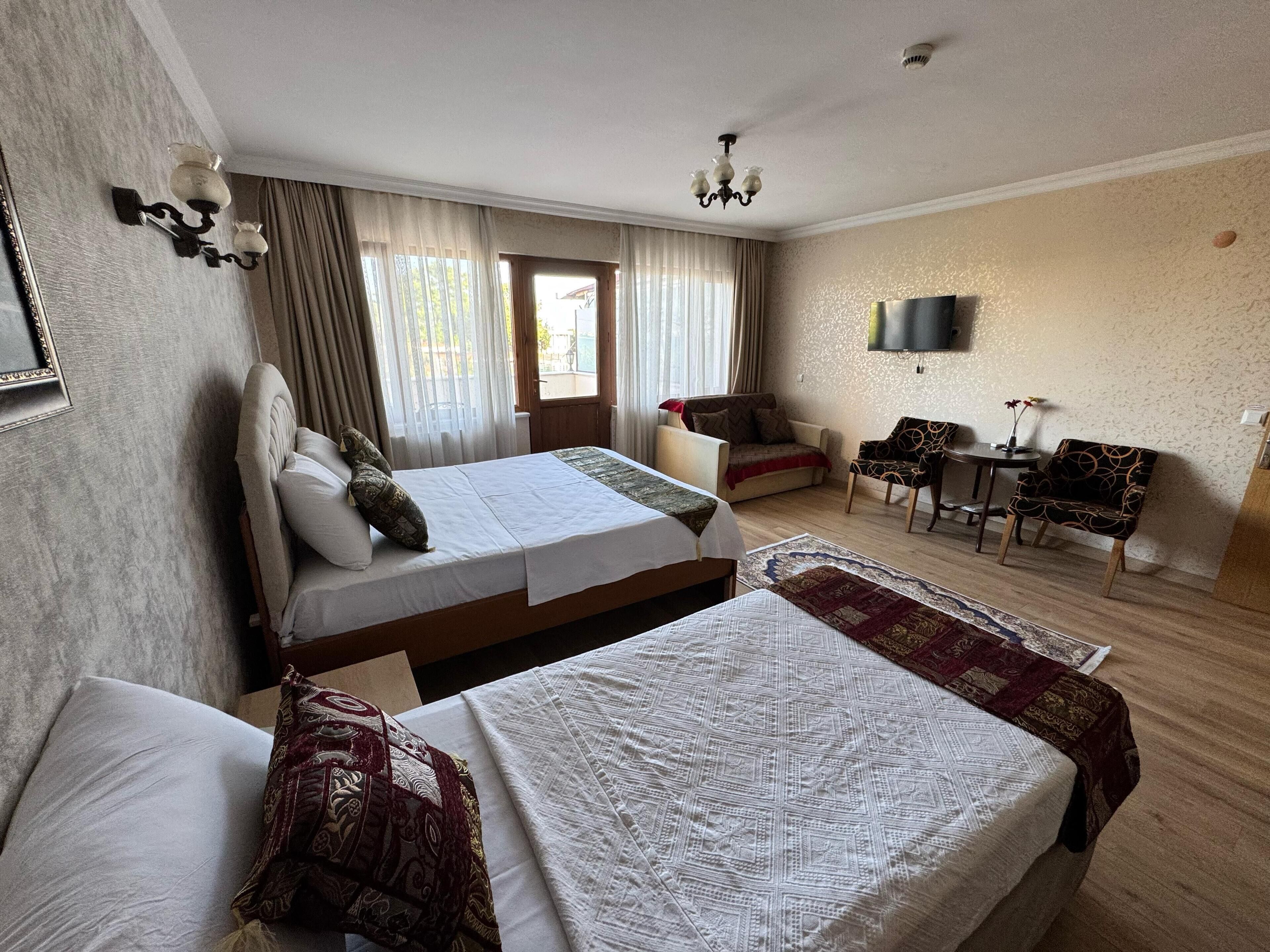 A hotel room with two beds, a desk, a chair, a TV, and a window with curtains.