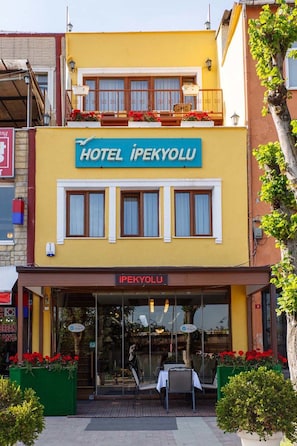 A two-story building with a sign reading "HOTEL İPEKYOLU" and a balcony with red flowers.
