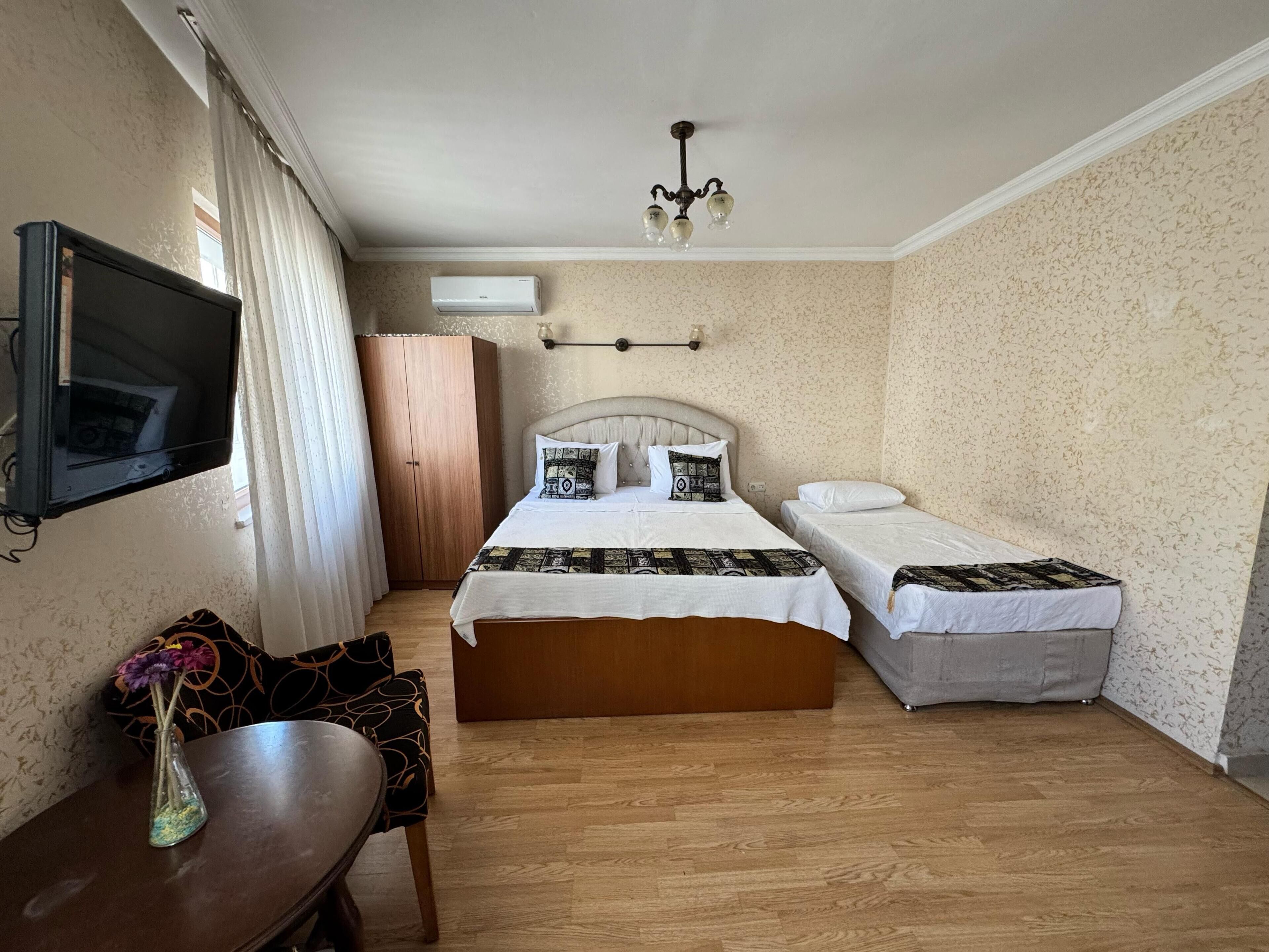 A hotel room with two beds, a TV, a desk, a chair, a vase with flowers, and a wardrobe.