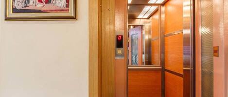 Interior de un ascensor con puerta de madera, panel de control y suelo alfombrado.