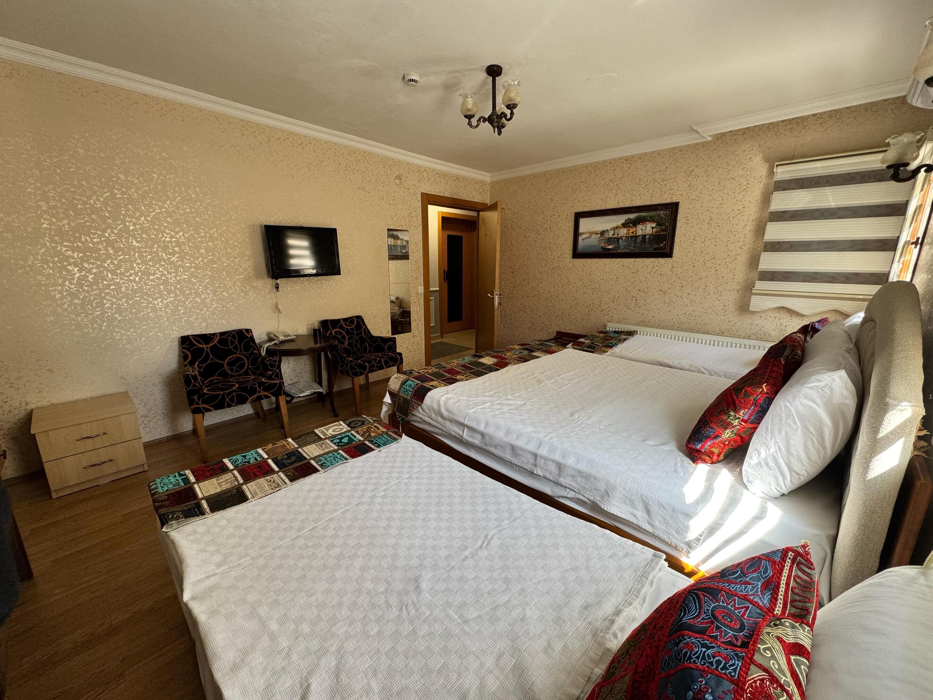 Une chambre d’hôtel avec deux lits, un bureau avec des chaises, un téléviseur à écran plat, un miroir et une fenêtre avec des stores.