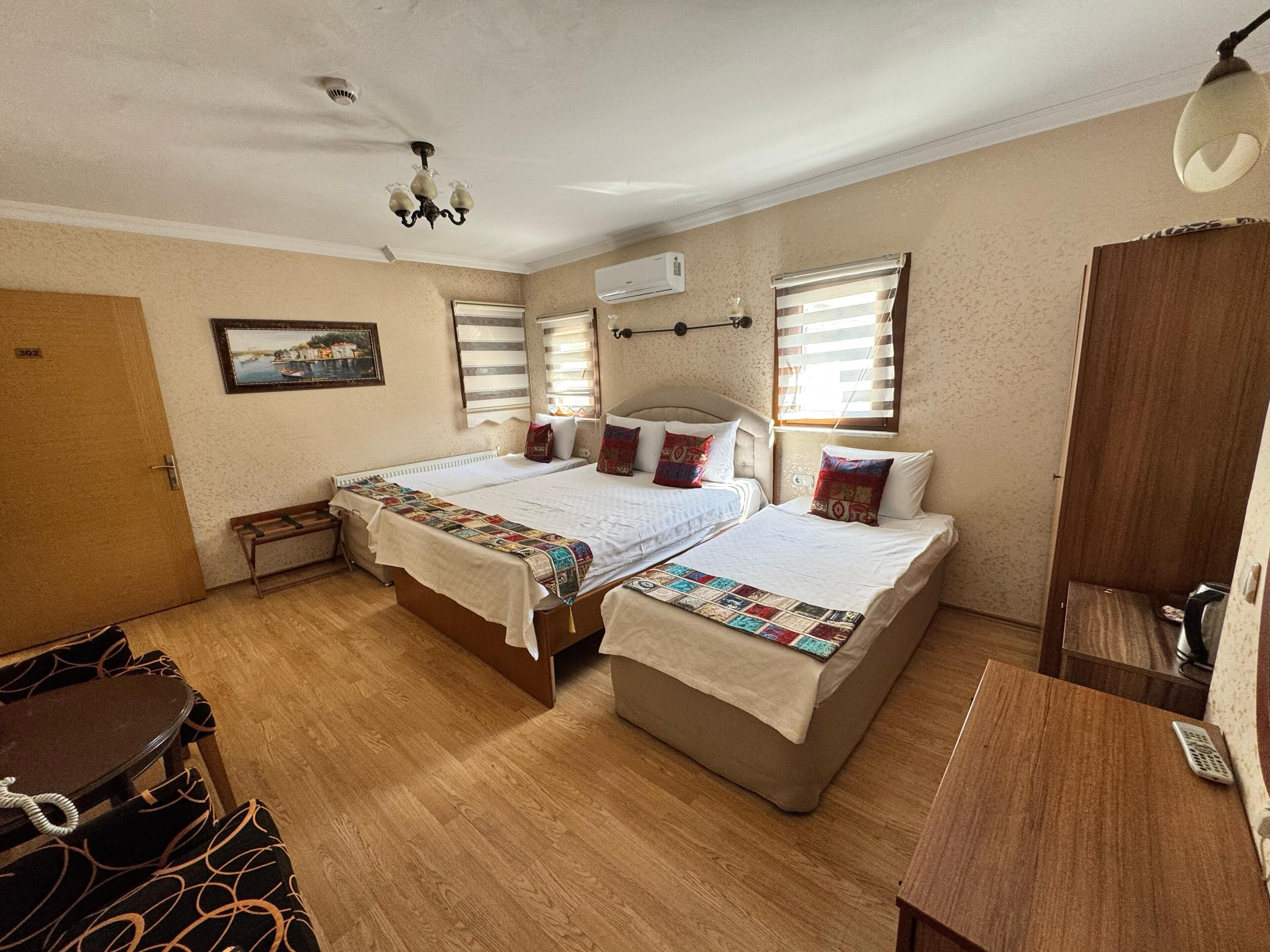 A room with two beds, a wooden bench, a small table, and a ceiling fan.