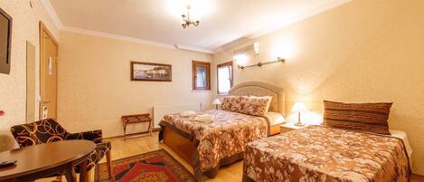 A hotel room with two beds, a dining table, chairs, a red patterned rug, and a painting on the wall.