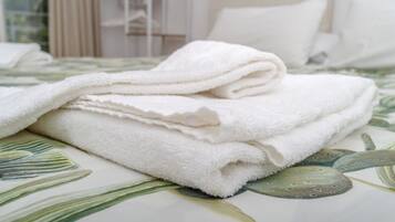 Una toalla blanca doblada con cuidado sobre una cama con una colcha estampada con motivos florales.