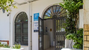 Une entrée d’immeuble avec une allée fermée par un portail, un panneau indiquant un espace de stationnement et un autre panneau précisant que le service de stationnement est disponible 24 heures sur 24.