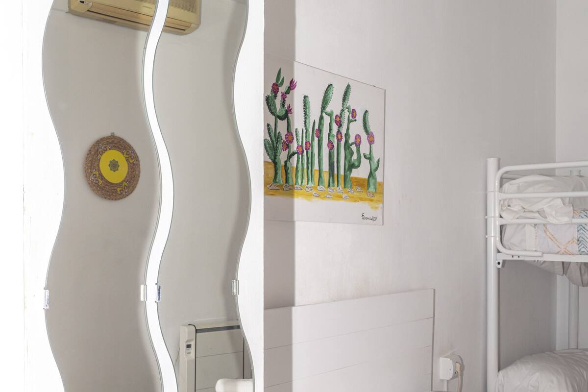 Ein Zimmer mit zwei Betten, einem Bild von Kakteen, einem Spiegel und einer Wandklimaanlage.