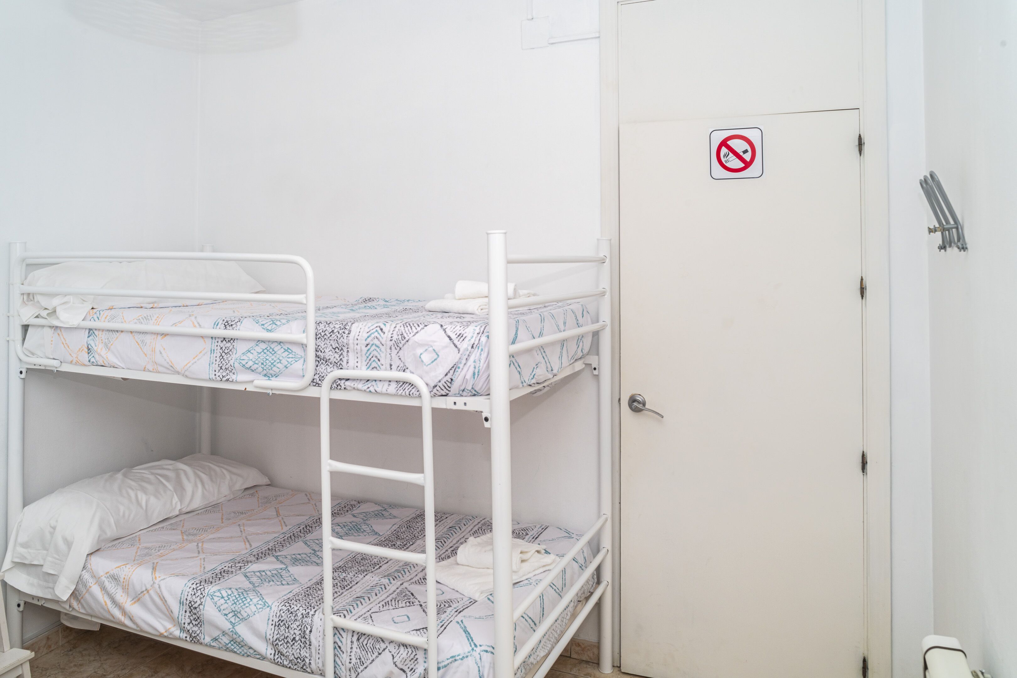 Habitación con literas, una puerta blanca y un cartel de no fumar.
