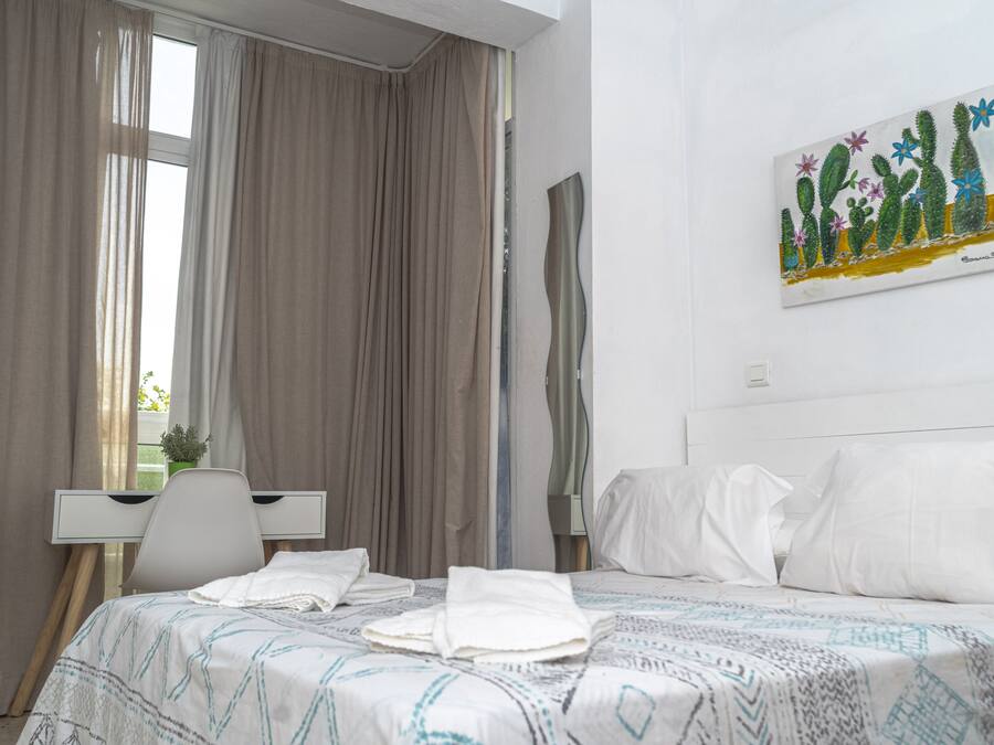 A hotel room with a bed, a desk, and a painting of cacti on the wall.