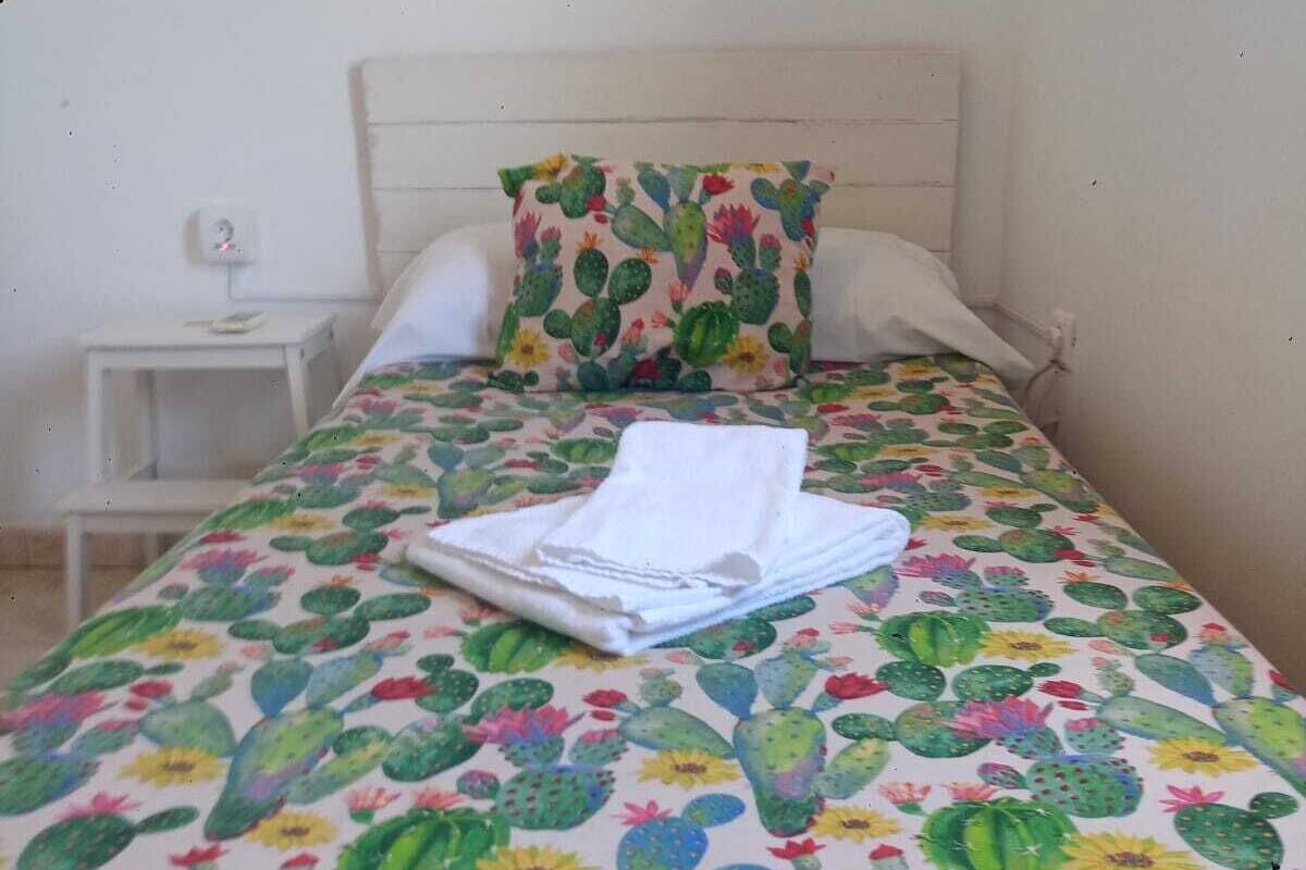 Ein Bett mit einer blumigen Tagesdecke, einem Kopfkissen und einem gefalteten weißen Handtuch.