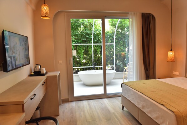 A modern bedroom with a large sliding glass door leading to a balcony, a bed, a desk with a computer, and a view of greenery outside.
