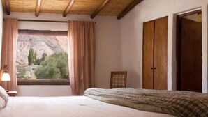 Un dormitorio con cama, ventana con cortinas, armario de madera y un espejo en la pared.