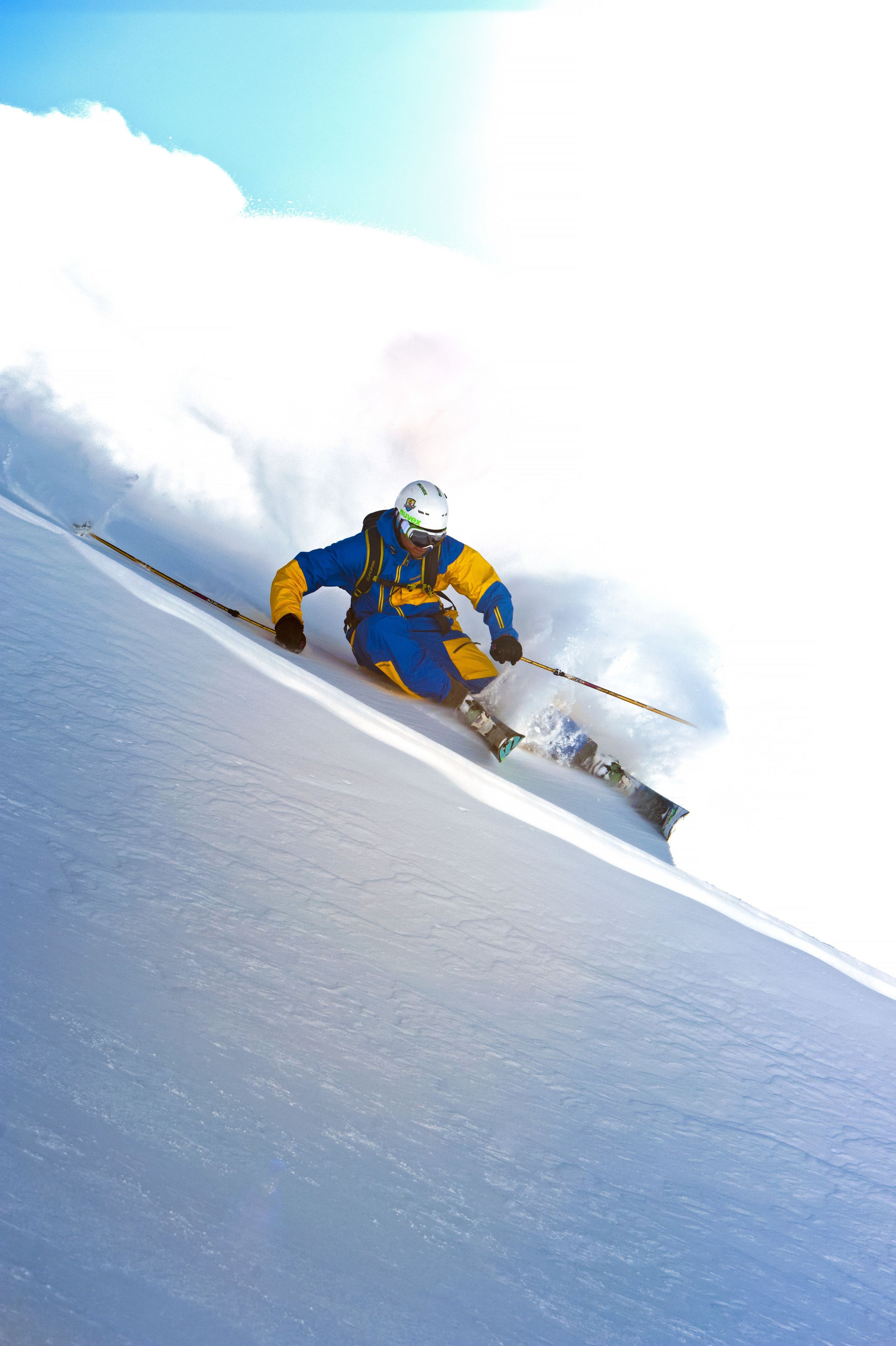 A skier in blue and yellow gear skiing down a snowy slope.