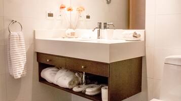 A modern bathroom with a white sink, mirror, and toilet. There are towels and toiletries on the counter.