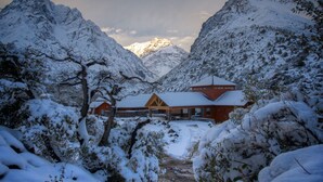 A snow-covered mountain lodge with a red building and a wooden structure in the foreground. - Noi Puma Lodge (Machalí)