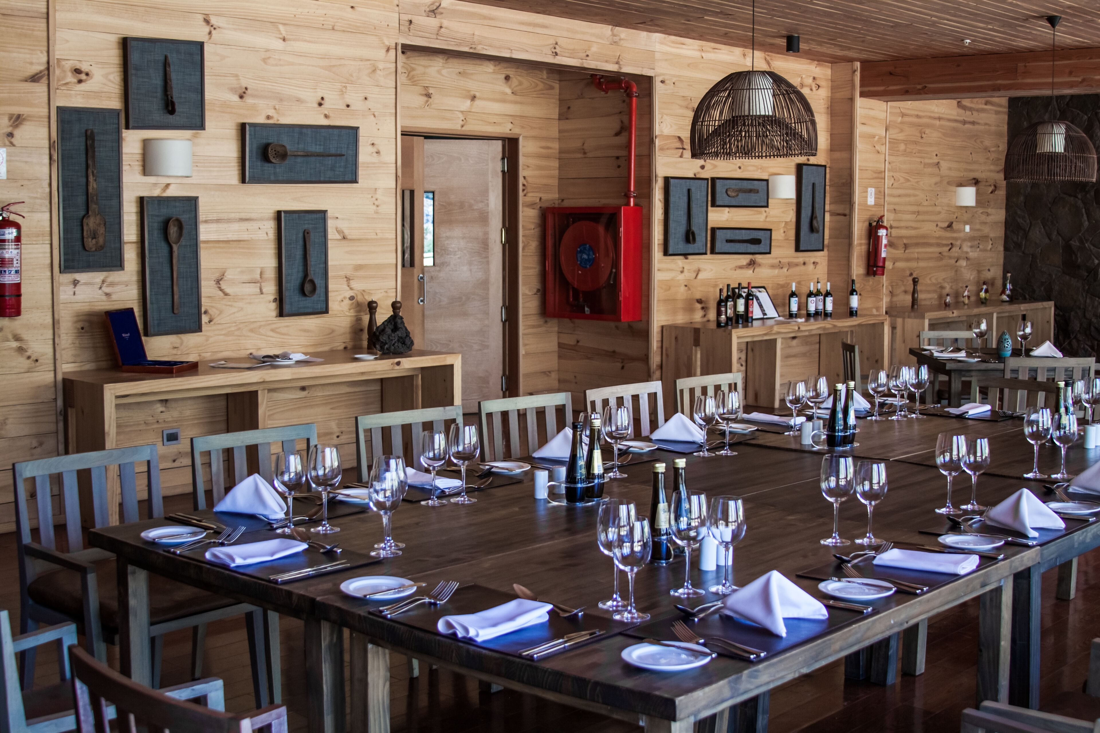 A long wooden dining table set for a meal, with chairs around it, in a room with wooden walls and a stone accent wall.