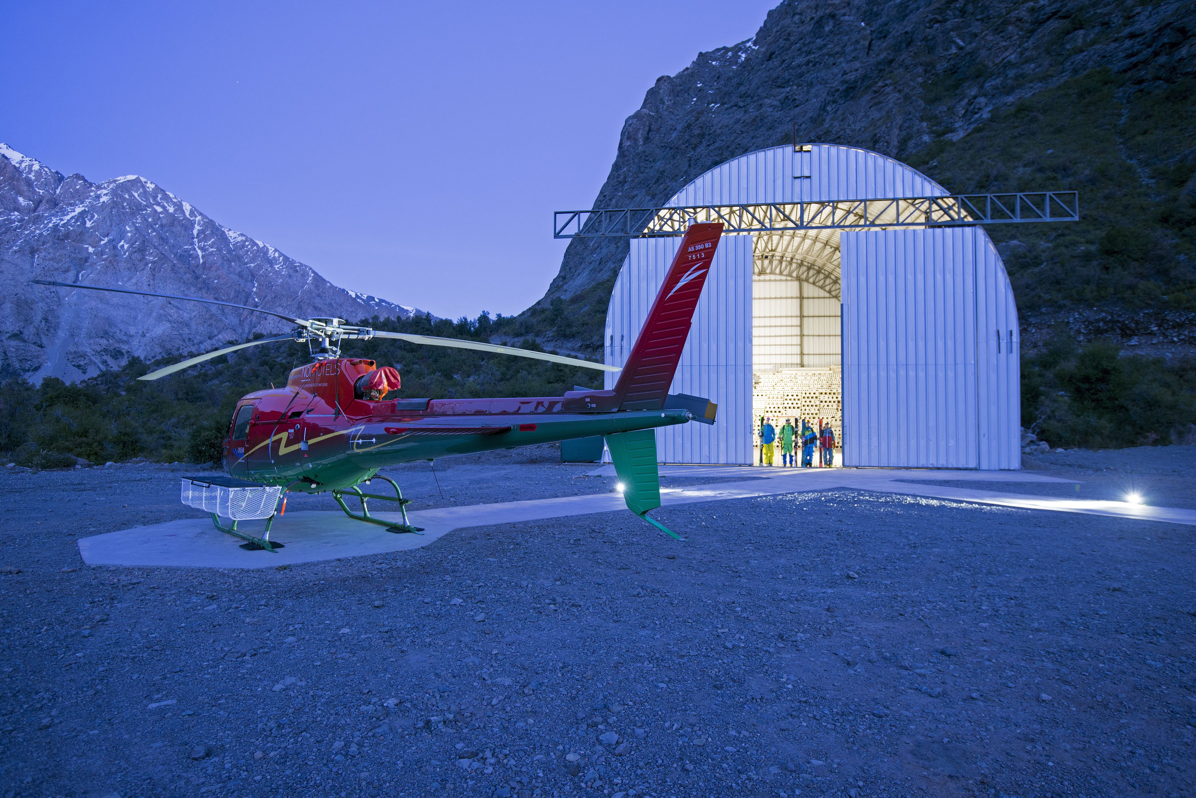Un helicòpter estacionat davant d'un edifici gran amb estructura metàl·lica i cua vermella.