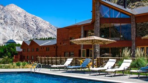 A modern building with a pool area, including lounge chairs and umbrellas, set against a mountainous backdrop. - Noi Puma Lodge (Machalí)
