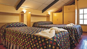 A room with three beds, wooden walls, and a sloped ceiling.