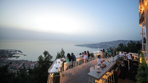 A rooftop terrace with tables and chairs overlooking a coastal cityscape. - Bay Lodge (Jounieh)