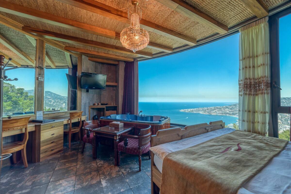 A room with a large window, wooden furniture, a chandelier, and a flat-screen TV.