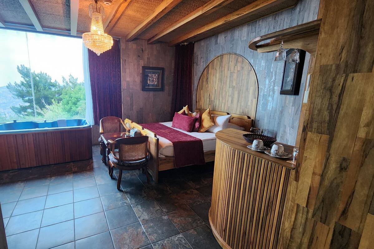 A cozy room with a bed, a wooden desk, and a window overlooking greenery.