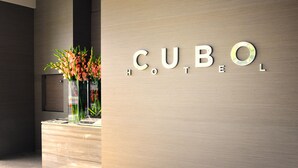 Modernilla designilla varustettu vastaanottotiski, jossa on lasivaasi kukkineen ja kyltti, jossa lukee: ”CUBO HOTEL”.