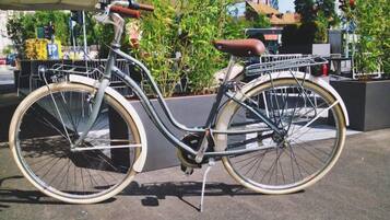Una bicicleta estática con canasta y asiento, estacionada en una acera.