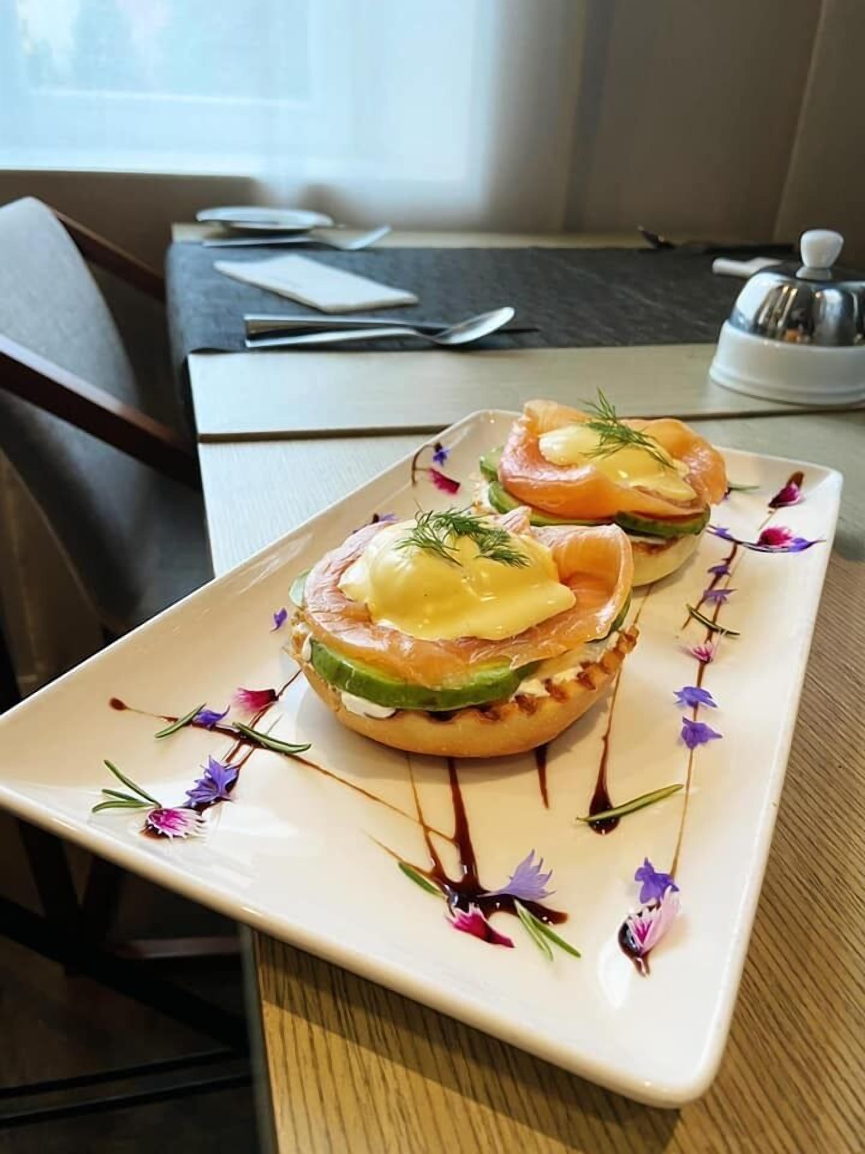 A plate with two open-faced sandwiches garnished with herbs, placed on a table with a napkin and a salt shaker.