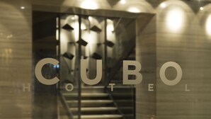 Hotellin sisäänkäynti, jossa on portaikko, joka johtaa aulaan, ja lasissa näkyy hotellin nimi: »CUBO HOTEL».