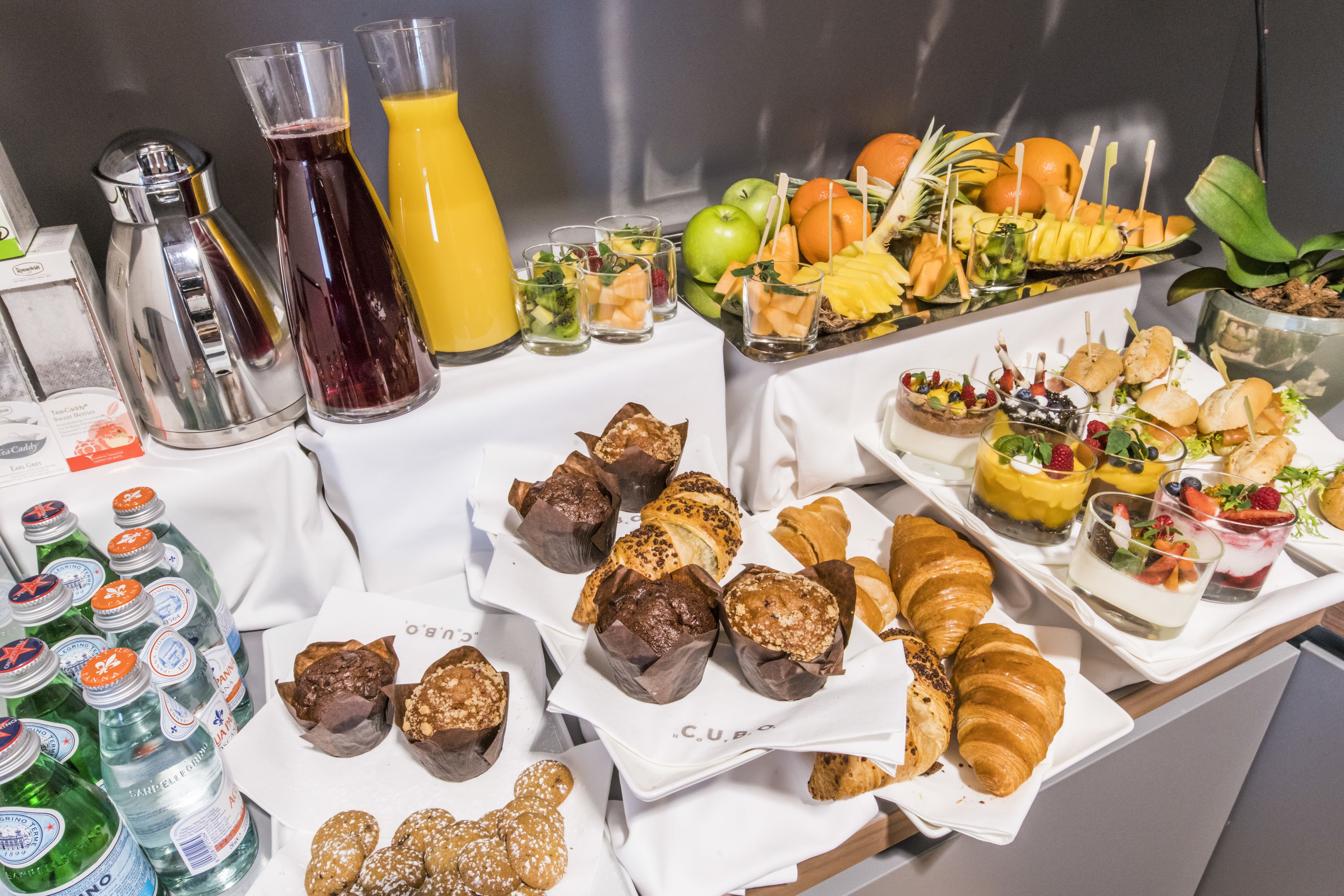 Un bufé con diversas opciones de comida, entre ellas pasteles, frutas y bebidas.
