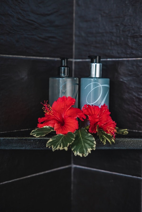 Deux bouteilles contenant un liquide, posées sur une étagère noire, avec des fleurs d’hibiscus rouges.