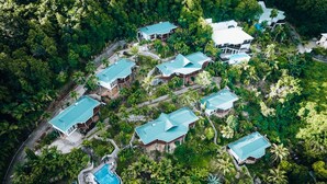 Luchtbeeld van een resort met meerdere gebouwen, een zwembad en weelderige begroeiing.