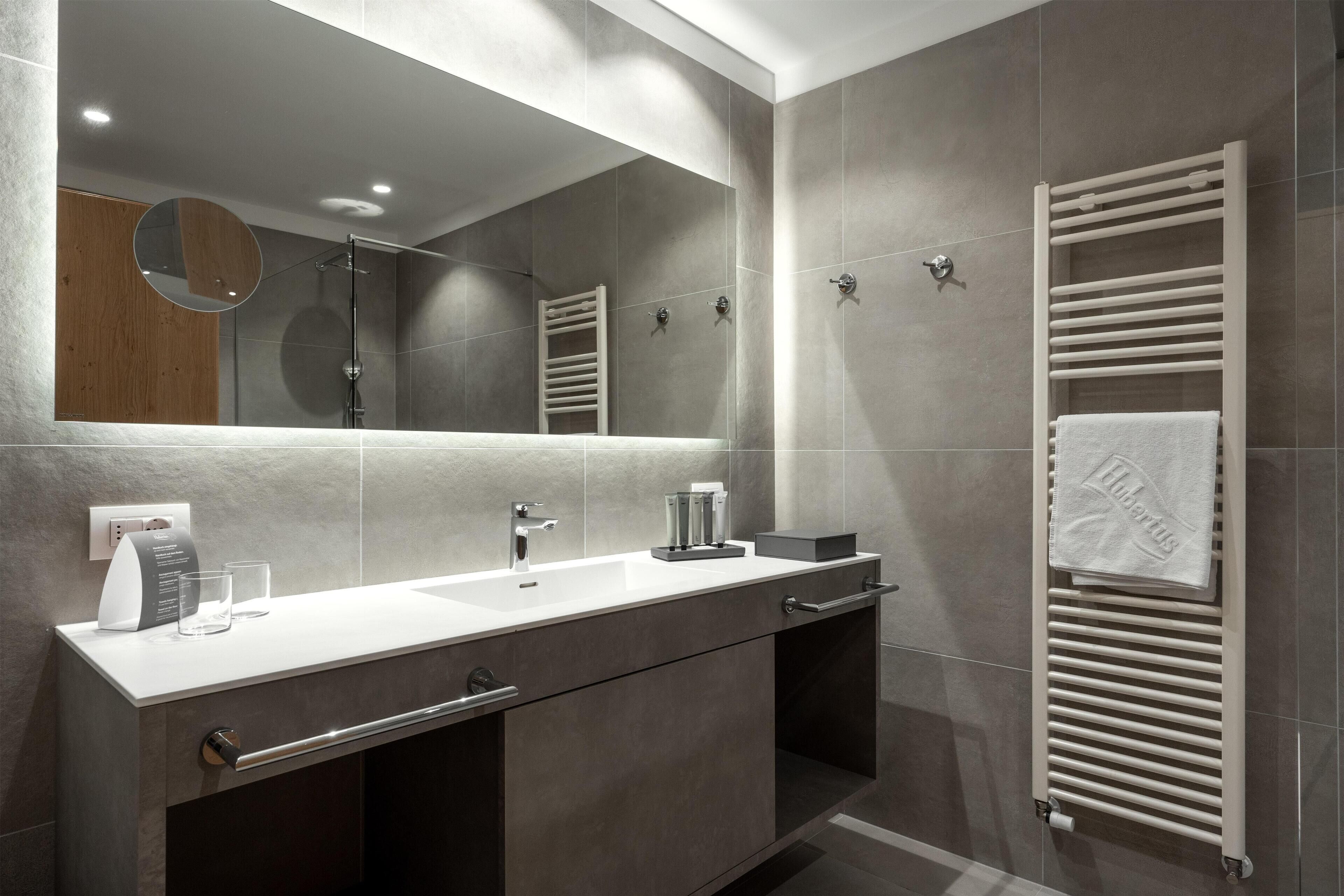 A modern bathroom with a large mirror, a white sink, and a towel rack.