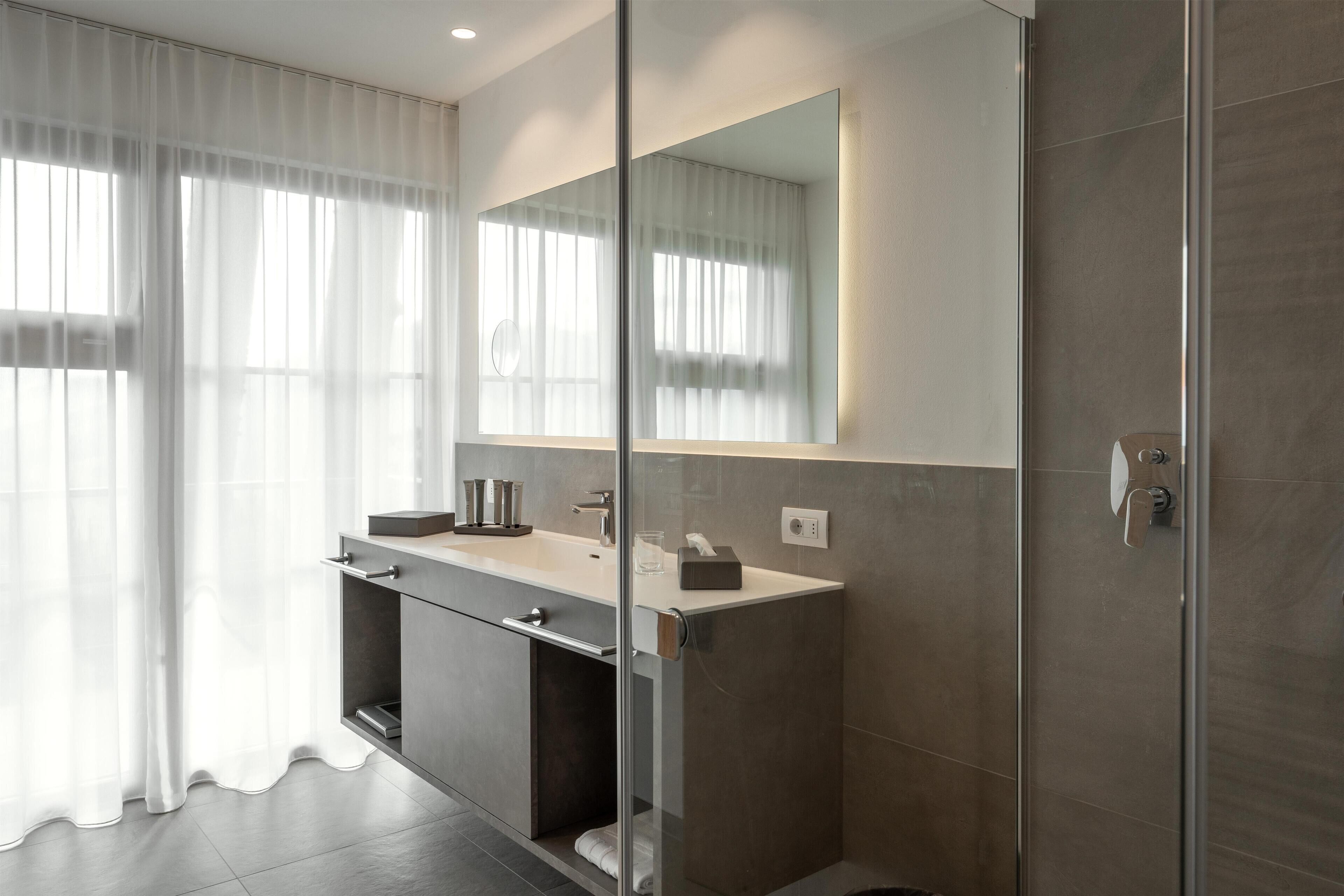 A modern bathroom with a glass shower enclosure, a large mirror, and a vanity with a sink and towel rack.