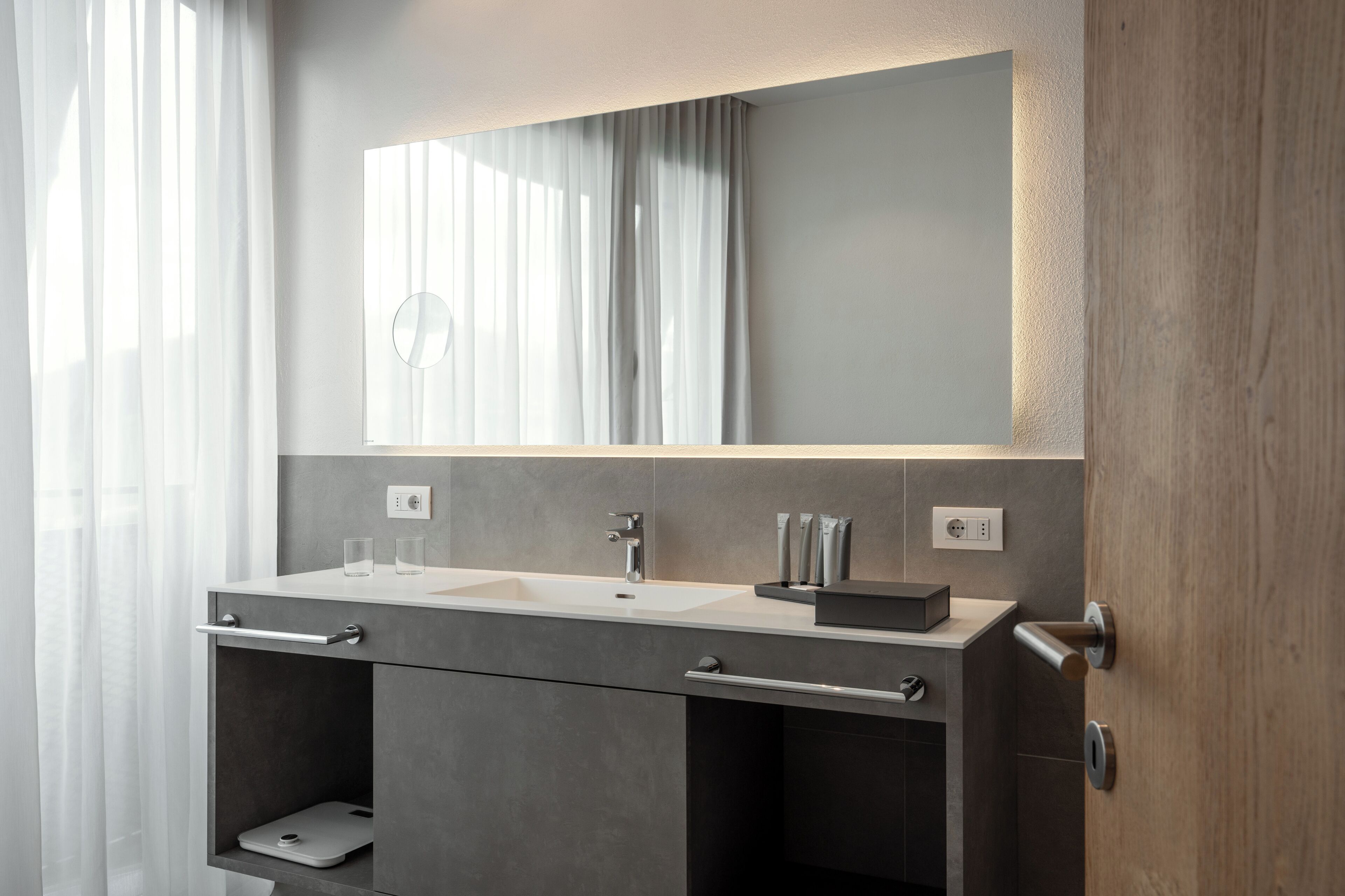 Un baño moderno con un espejo grande, un lavabo y un mueble con cajones.