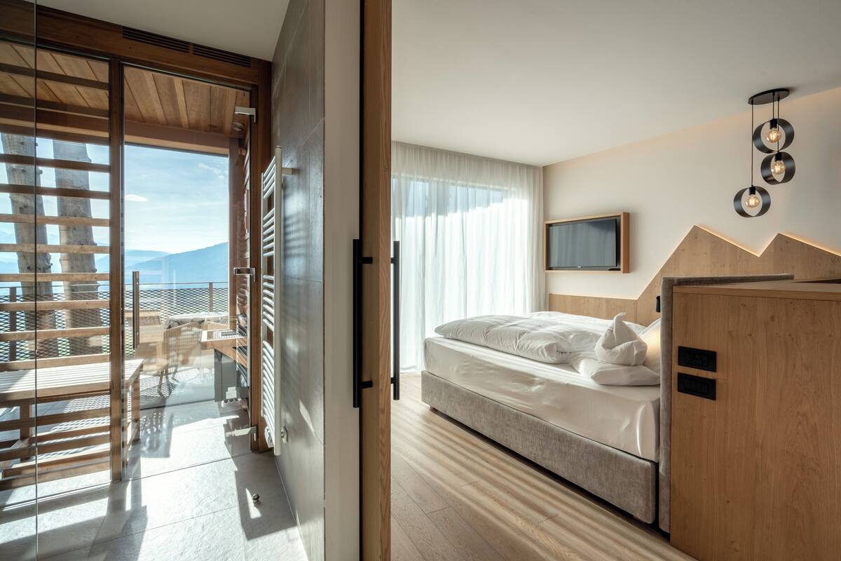 A modern bedroom with a bed, a TV, and a view of the outdoors.